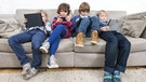Vier Kinder sitzen auf der Couch und beschäftigen sich mit Laptop, Tablet und Smartphone. | Bild: stock.adobe.com/Corepics