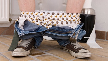 Füsse eines Mannes, der mit heruntergelassener Hose auf dem Klo sitzt | Bild: colourbox.com