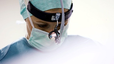 Eine Chirurgin operiert mit einer Lichthaube am Kopf | Bild: picture-alliance/dpa