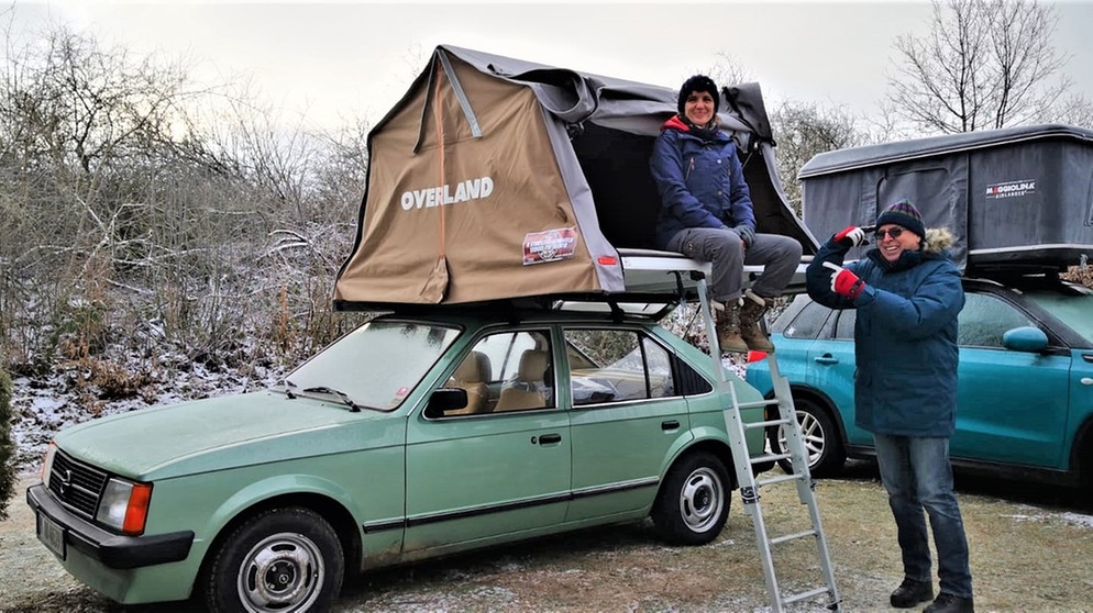 Bernd Gierstner (Kameramann) zeigt Sylvie Menning (Autorin) einen Vogel, für die Idee, im Winter im Dachzelt auf dem Opel zu übernachten… Eifel, 2019. | Bild: BR