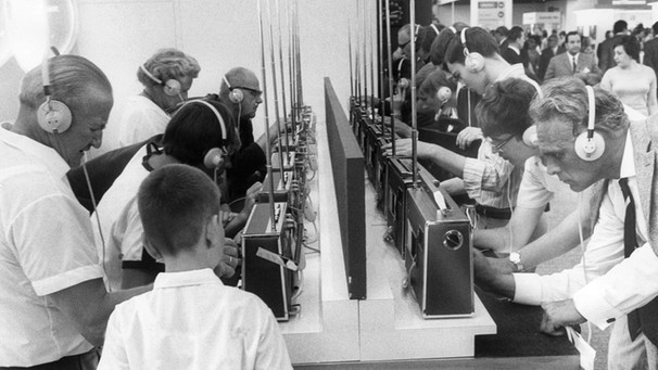 Viele Menschen stehen mit Kopfhörern an einem Messetrand mit Kofferradios | Bild: dpa/Konrad Giehr
