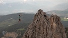 Mann auf einem Slackline-Seil zwischen zwei Berggipfeln in schwindelerregender Höhe schwingt die Peitsche zum Goaßlschnalzen | Bild: Rai Südtirol
