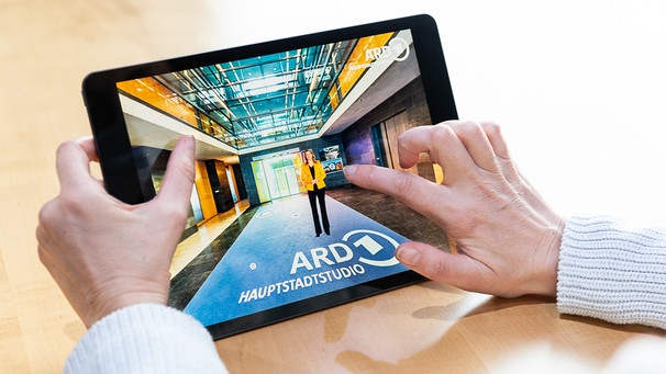 Hände halten Tablet, auf dem Display Einblick in das ARD-Hauptstadtstudio | Bild: ARD-Hauptstadtstudio/Christopher Domakis