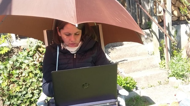Margit Ringer sitzt im Garten unter einem Schirm und schreibt mit Nootebook | Bild: privat