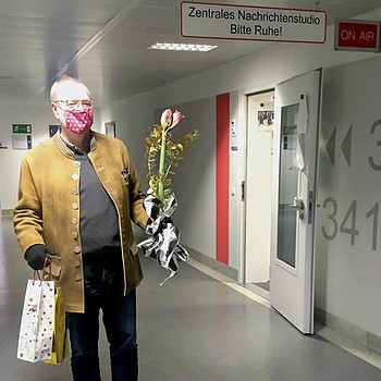 Martin Fogt mit Maske vor dem BR Nachrichtenstudio mit Amaryllis in der einen Hand und einer Flasche Wein in Geschenktasche in der anderen. | Bild: BR/Karin Schumacher