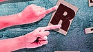 Illustration/Collage: Viele einzelne Scrabble-Buchstaben, links vier Arme, deren Zeigefinger auf einige Buchstaben zeigen | Bild: colourbox.com; BR/Tanja Begovic
