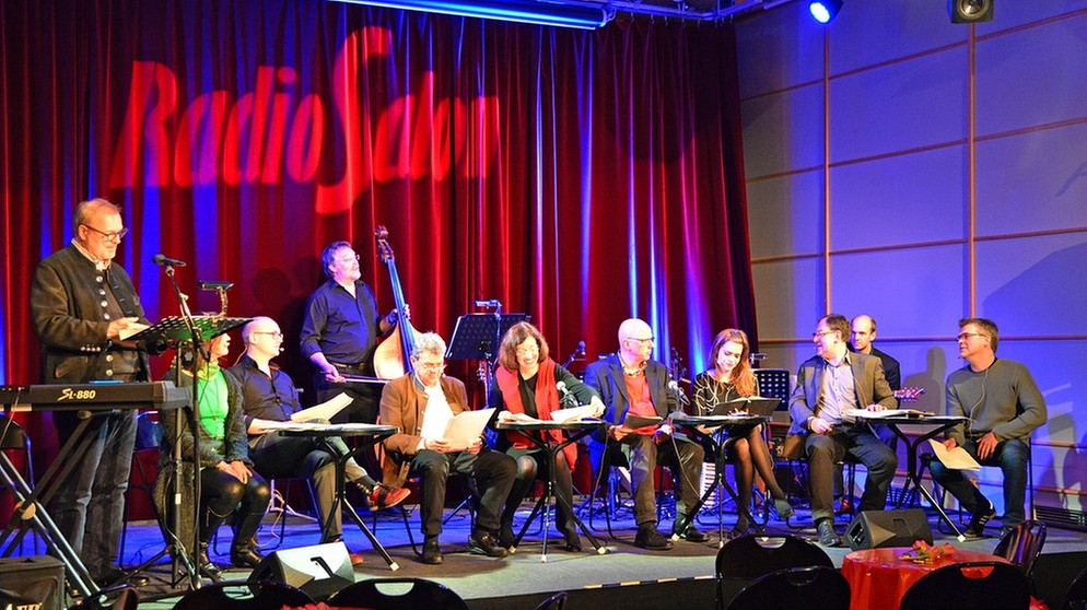 Das Sprecher-Ensemble sitzend auf der Bühne bei der Probe zur Sprecherstunde | Bild: BR/Susanne Kolibius