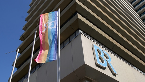 Eine Regenogenfahne mit dem BR-Logo weht vor dem BR-Hochhaus. | Bild: BR