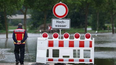 03.06.2024, Bayern, Asbach-Bäumenheim: Ein Feuerwehrmann steht an einer vom Hochwasser überfluteten Straße: | Bild: dpa-Bildfunk/Karl-Josef Hildenbrand