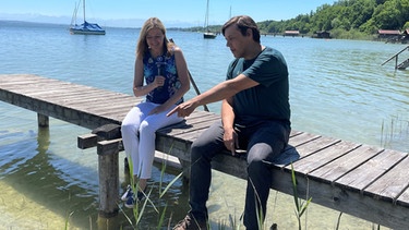 Iska Schreglmann interviewt Thassilo Franke sitzend auf einem Steg am See  | Bild: Bernhard Kastner