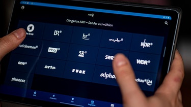 Ein Mann benutzt die ARD-Mediathek App auf einem Tablet, auf dem unter anderem die Sender BR, hr, mdr, NDR, phoenix, rbb, SR, SWR, WDR und arte zu sehen sind. | Bild: dpa-Bildfunk/Fabian Sommer