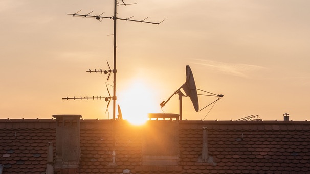 Die Sonne geht hinter einem Dach mit einer Satellitenschüssel auf. | Bild: Marie Reichenbach / dpa picture alliance