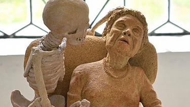 Skelett-Figur umgreift Figur einer älteren sitzenden Dame / Ausstellung "Totentanz" in der Kartause Buxheim | Bild: Manfred Mühlbauer