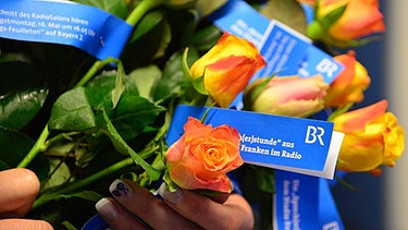 Ein Strauß orange-gelber Rosen mit BR-blauen Sprecherstunden-Banderolen | Bild: BR/Susanne Kolibius