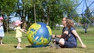 Zwei Erwachsene spielen mit einem Kind Ball. | Bild: Nicolaidis Young Wings Stiftung