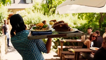 Kellnerin trägt ein Serviertablett mit Speisen. | Bild: BR